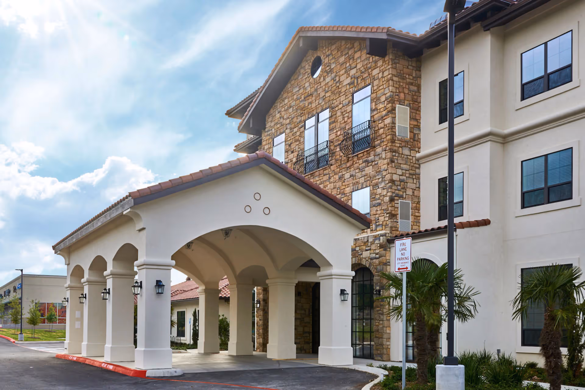 Covered porte-cochere entrance of a multi-story building with stone and stucco facade and palm trees.