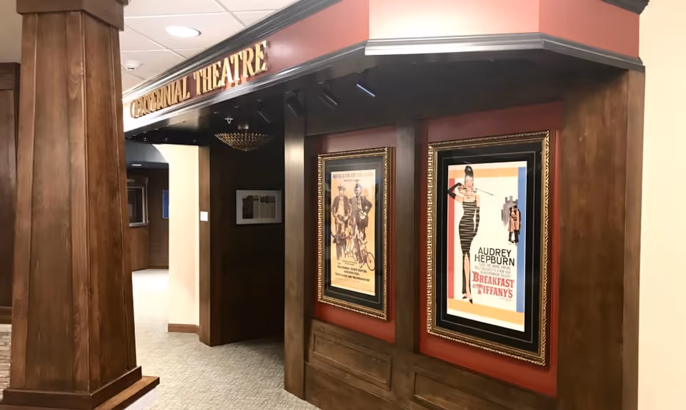 Entrance to a small theater hallway with wood-paneled columns and framed movie posters, including a 'Breakfast at Tiffany's' poster.