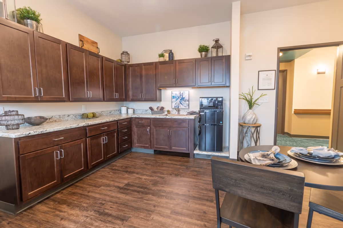 Bright kitchen area with dark wood cabinets, marble countertops, a small refrigerator and a set dining table.