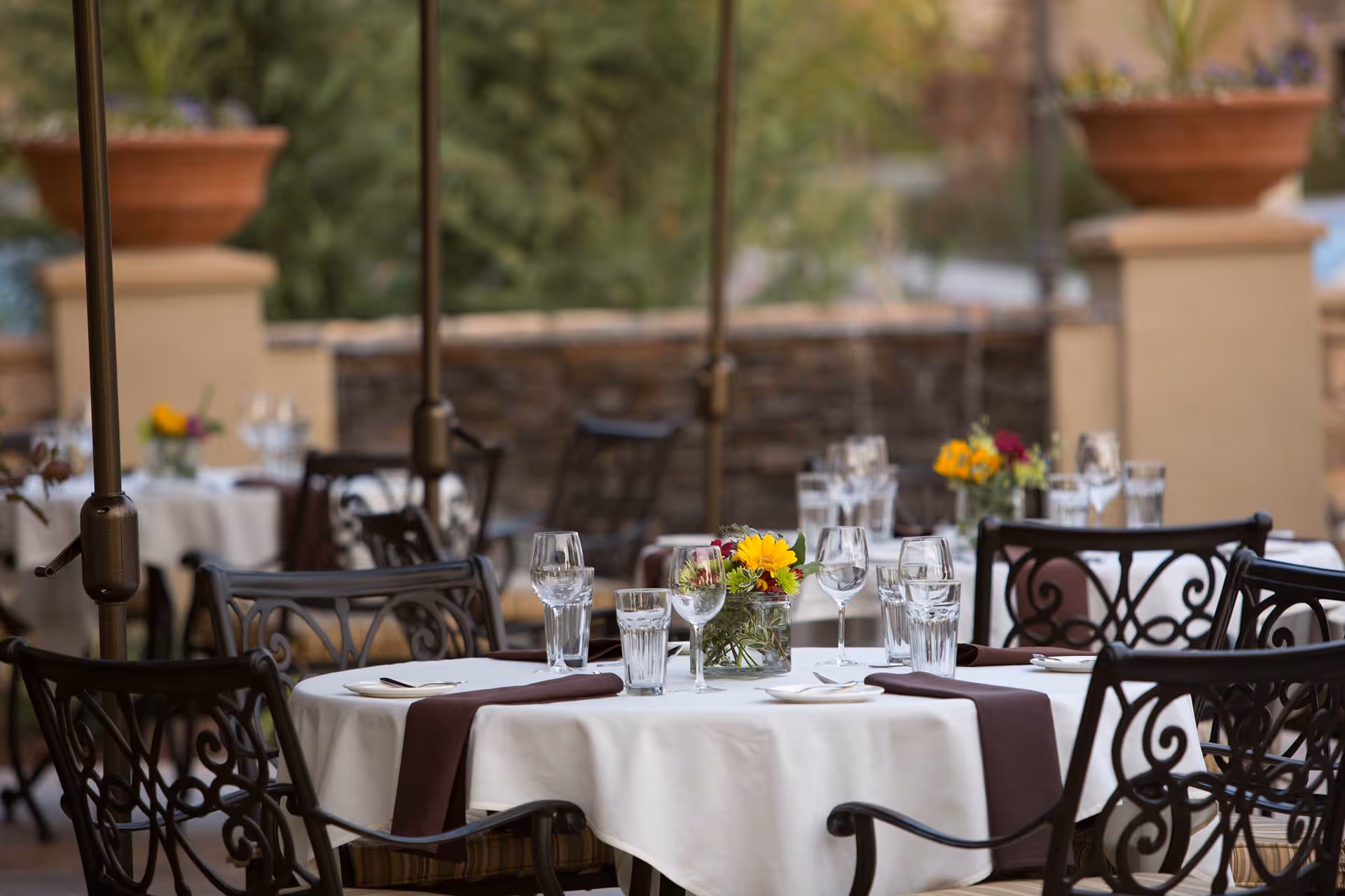 Outdoor patio dining area with round tables set with white tablecloths, glassware, and floral centerpieces.
