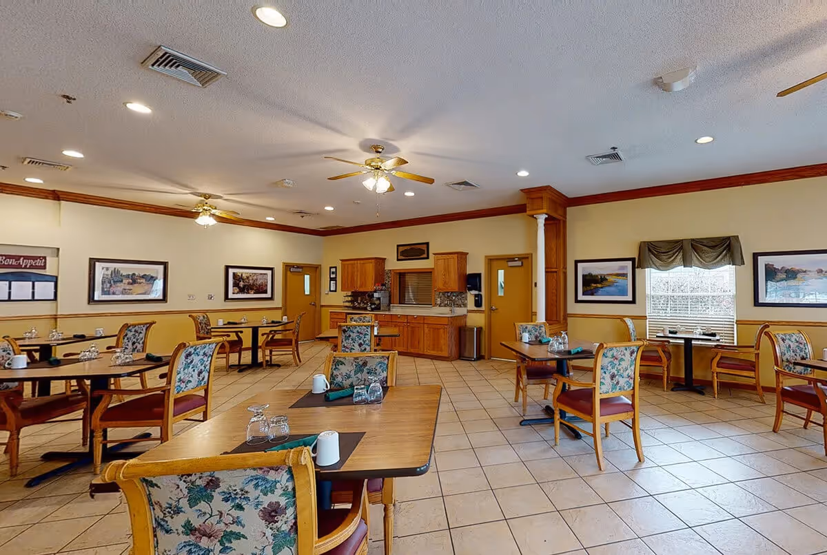 Spacious dining room with multiple tables and floral-upholstered chairs, a serving counter and framed wall art.