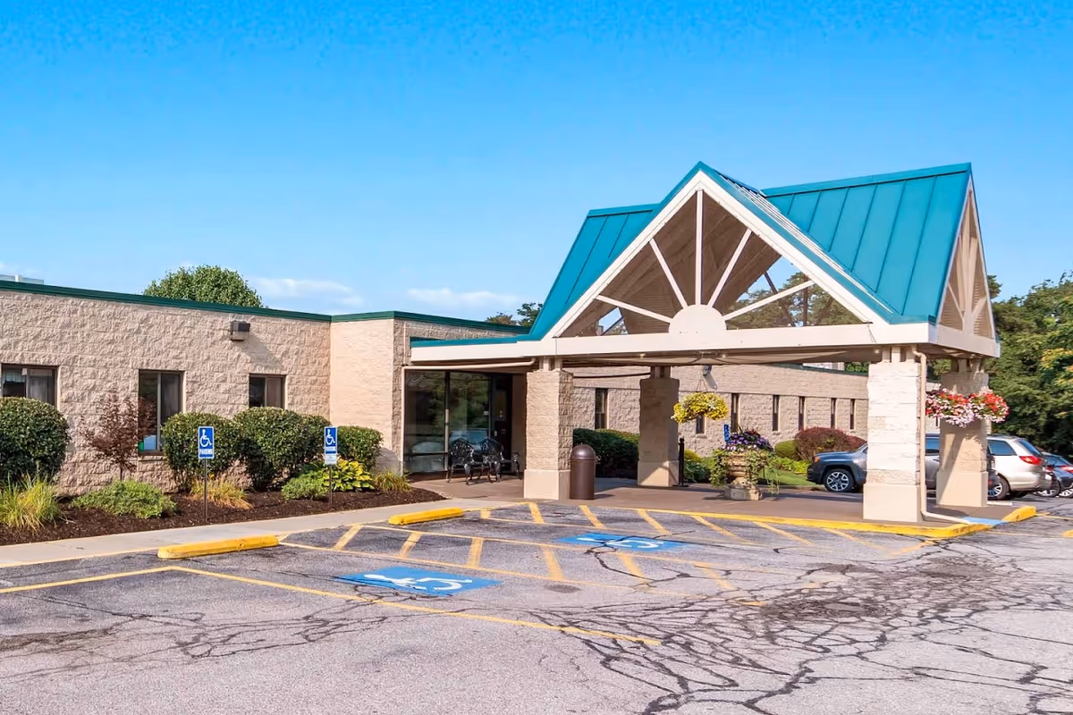 Entrance and covered porte-cochere of a single-story healthcare building with a teal peaked roof, handicap parking spaces and landscaped beds.