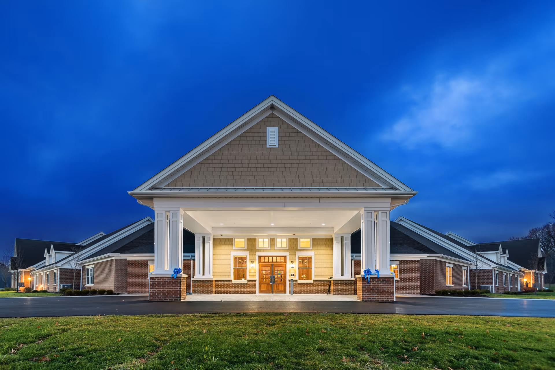 Front entrance of a brick assisted living building with a large covered portico lit at dusk.