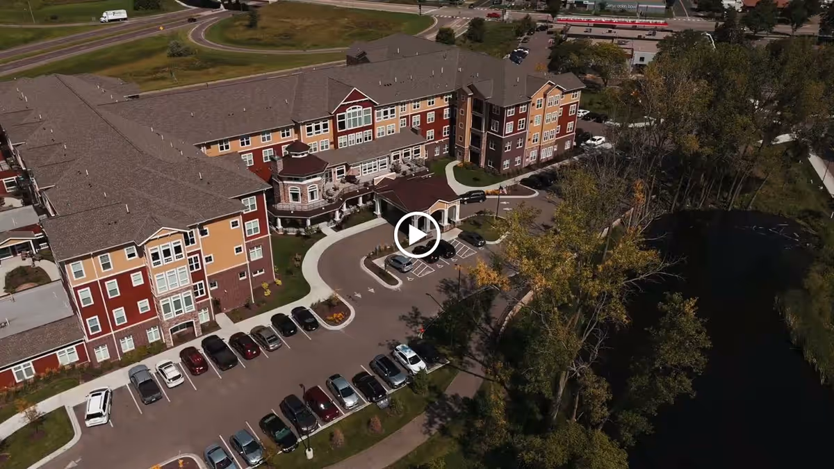 Aerial view of a multi-story senior living building with a parking lot and a pond alongside it.