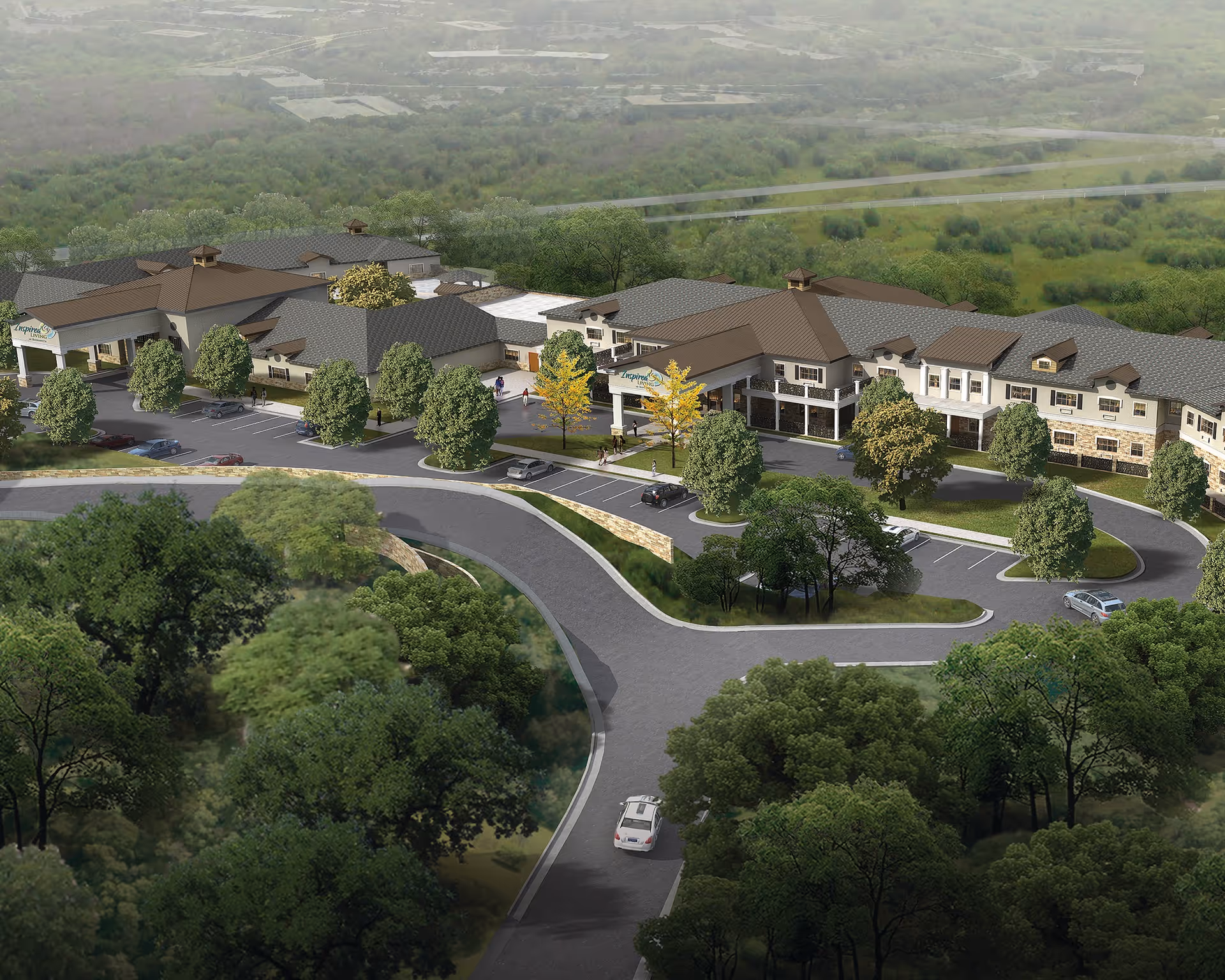 Aerial view of Inspired Living Alpharetta senior living facility surrounded by greenery and trees. The building has a large parking area with several cars and a curved driveway leading to the entrance. The facility features multiple connected buildings with pitched roofs and a covered entrance.