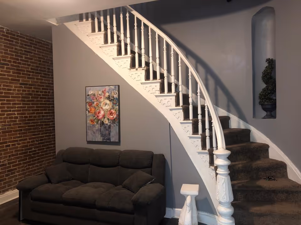 Curved white staircase beside a gray sofa in a cozy living area with brick wall.