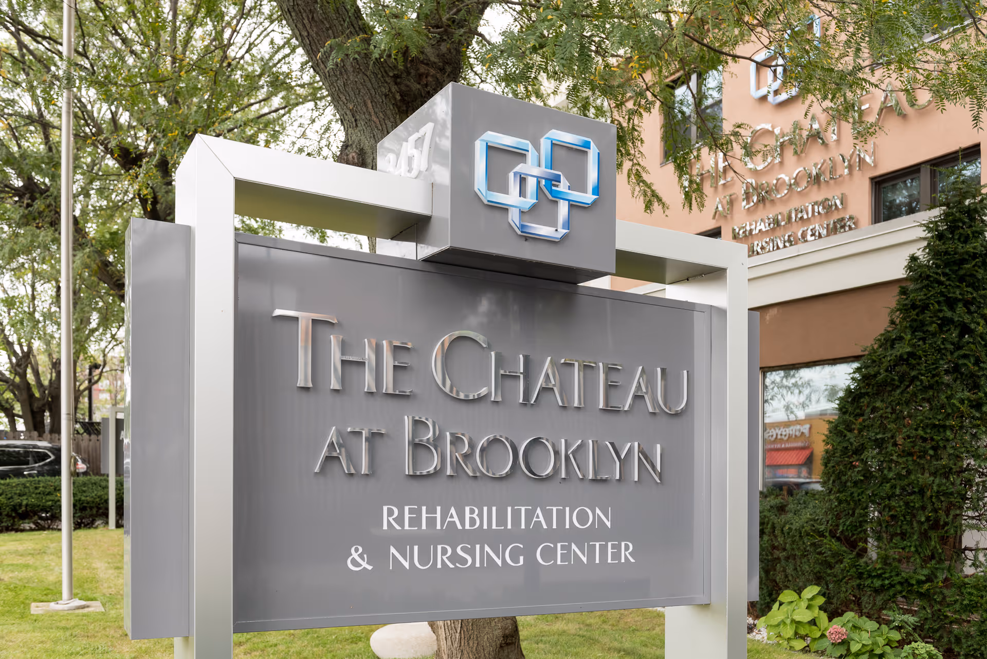 Outdoor view of a large sign for The Chateau at Brooklyn Rehabilitation & Nursing Center with trees and part of the building visible in the background.