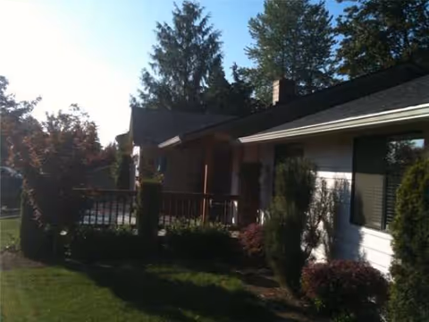 Exterior view of a single-story building with a deck and trimmed shrubs.
