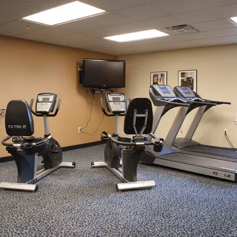 Small fitness room with recumbent exercise bikes, treadmills, and a wall-mounted TV.