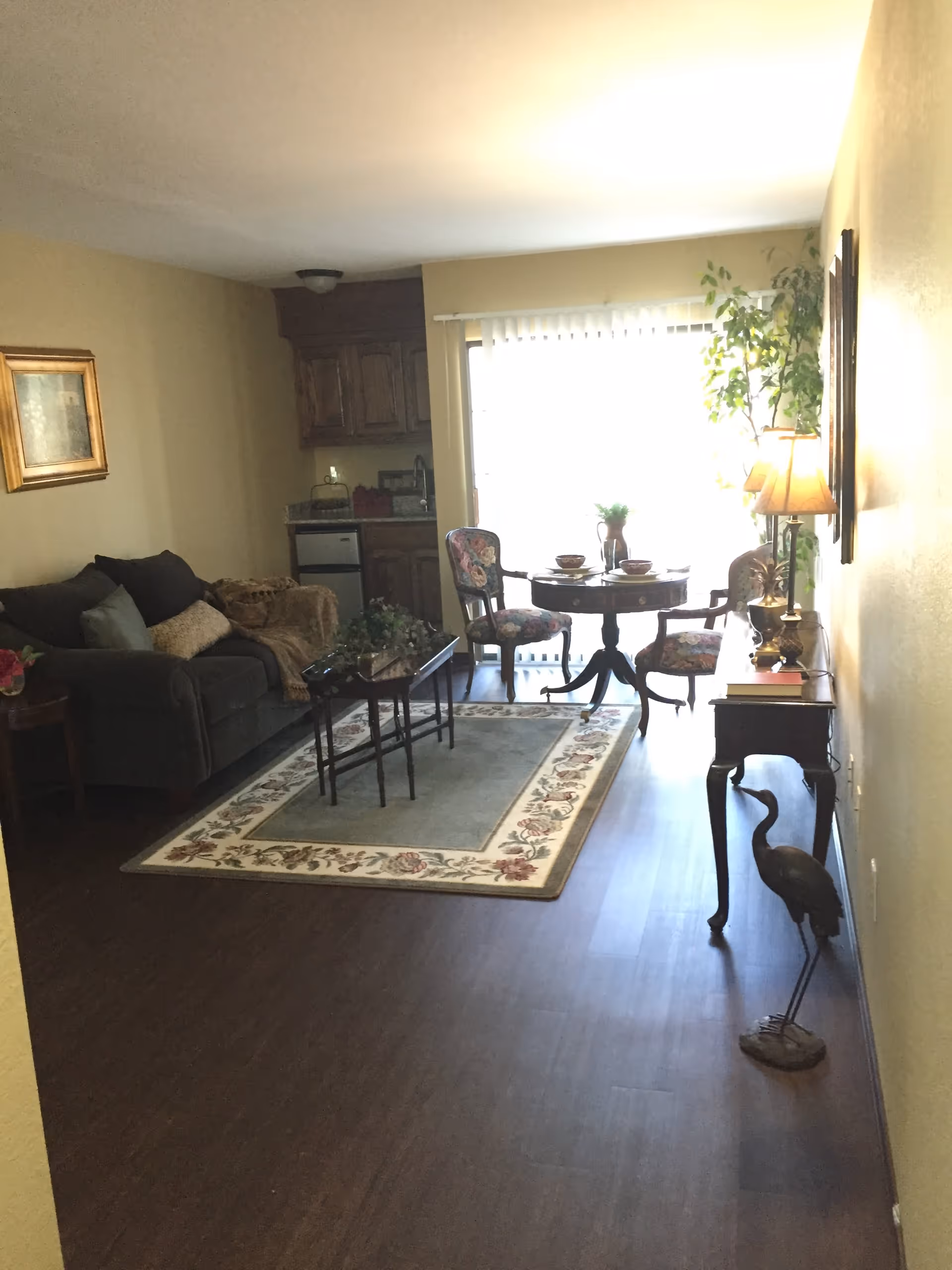 Living room with a sofa and coffee table on an area rug, a small round dining table by sliding glass doors, and a console table with a lamp.