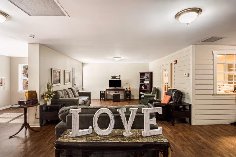 Communal living room with sofas, armchairs, a TV, and large decorative 'LOVE' letters on a bench.