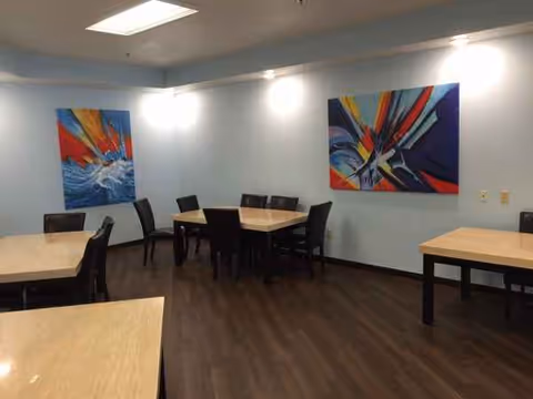 A light-blue walled dining area with tables, chairs, and colorful wall art.