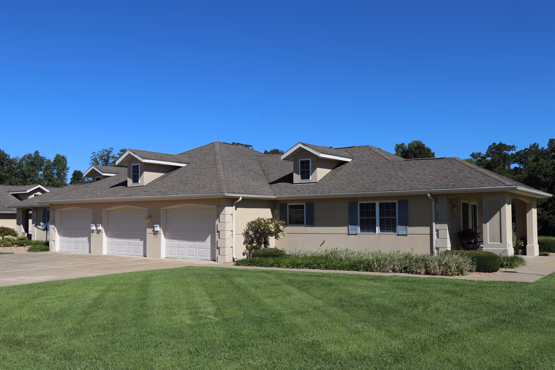 Single-story beige building with three garage doors, a manicured green lawn, and clear blue sky.