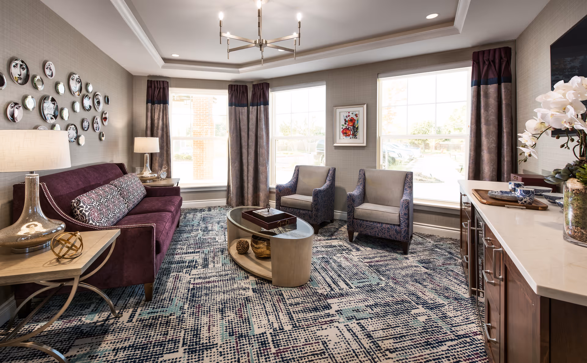 Bright furnished sitting room with a purple sofa, two armchairs, a coffee table, and large windows.