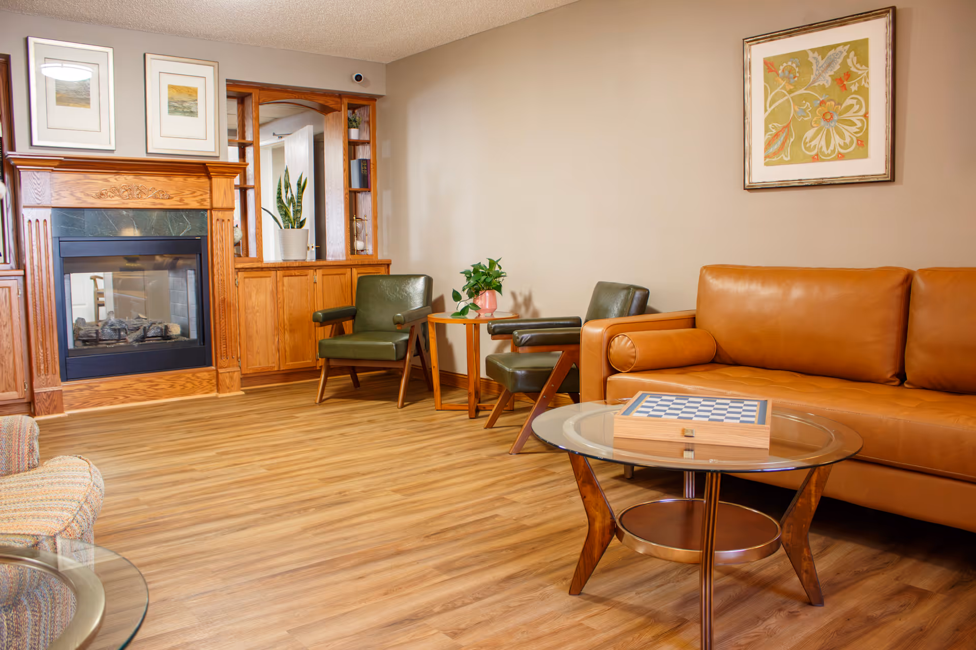 Comfortable living room with a leather sofa, green armchairs, a fireplace, and a glass coffee table with a chessboard.