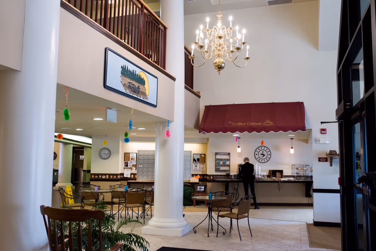 Lobby interior showing a coffee counter under a red awning, seating tables, tall white columns and a hanging chandelier.