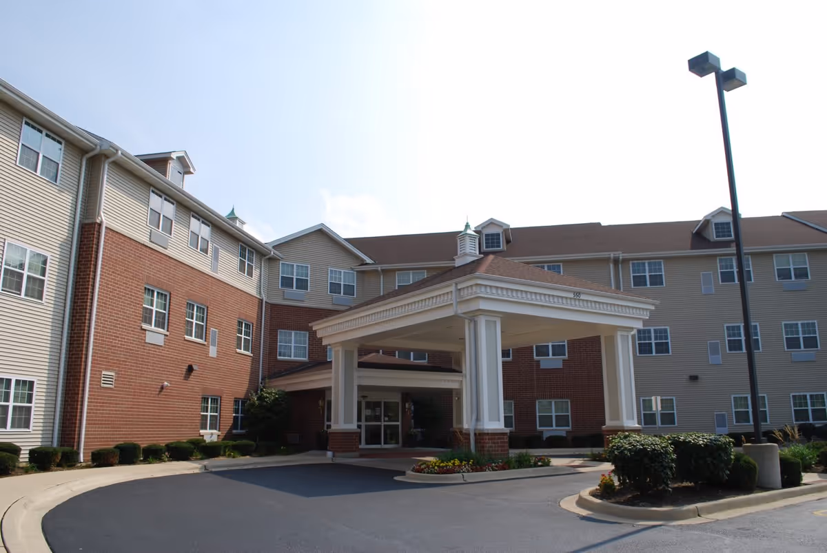 Entrance porte-cochère and driveway of a multi-story brick-and-siding senior living building with landscaping.