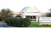 Front entrance of Schuyler Ridge Residential Healthcare with a covered entry, manicured shrubs, and a sign on the lawn.