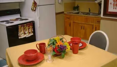 Dining table with yellow tablecloth, red dishes, and a kitchenette in the background.