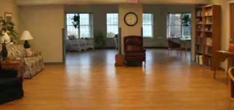 A spacious common lounge with chairs, sofas, a clock, and bookshelves.