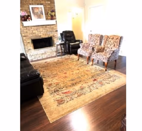 Cozy living room with brick fireplace, wooden floors, chairs, and a large rug.