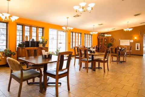 Bright dining room with wooden tables and chairs, large windows, and orange walls.