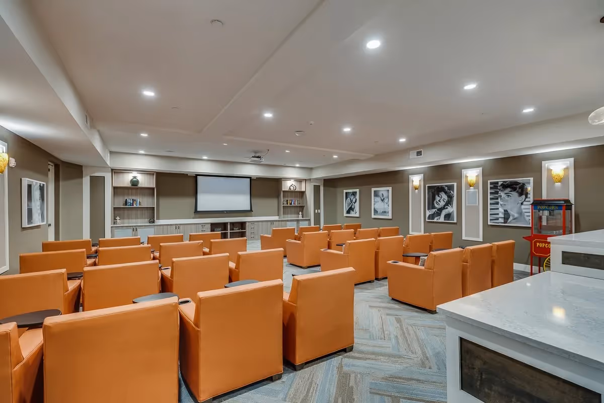 Community screening room with rows of orange armchairs facing a projector screen and a popcorn machine.
