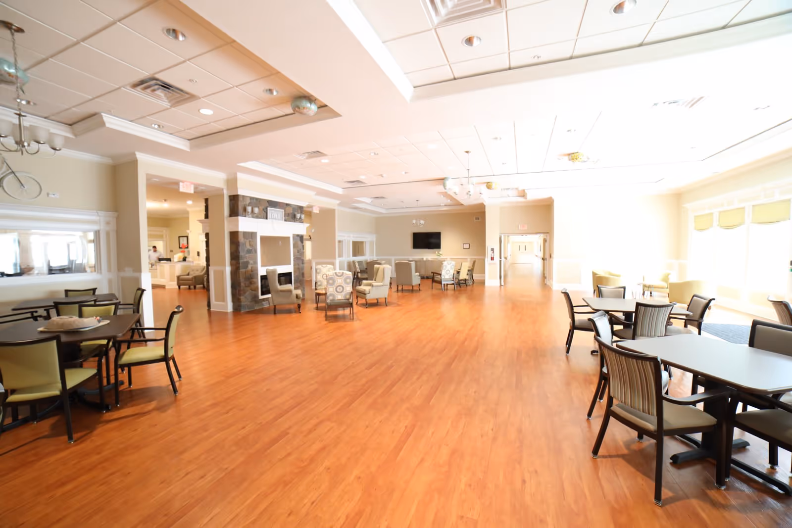 Large bright common dining area with multiple tables and chairs, lounge seating, and wood flooring.