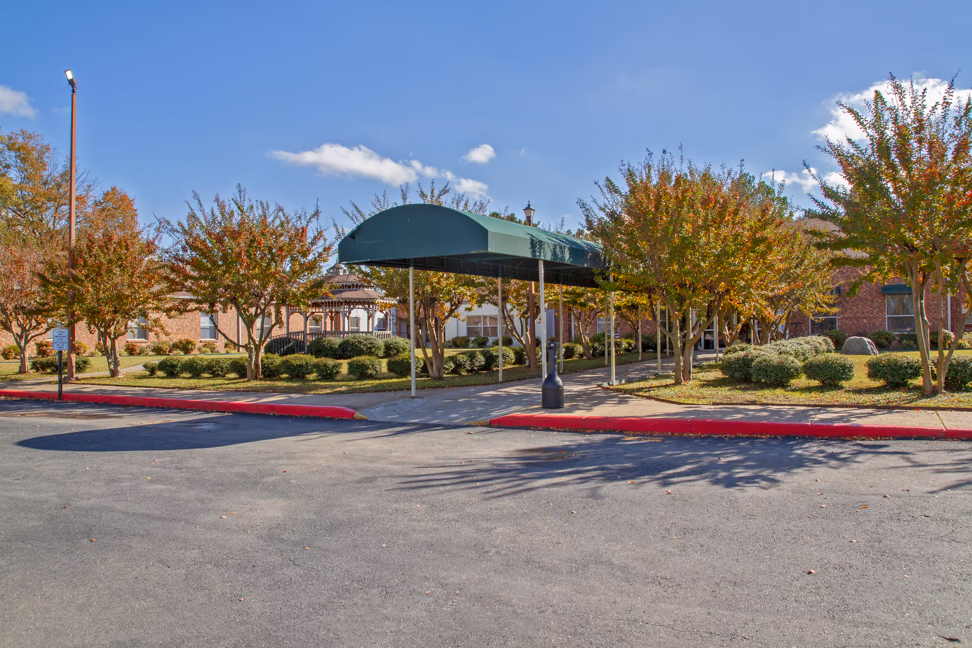 Covered entrance canopy and landscaped driveway in front of a brick nursing facility surrounded by trees.