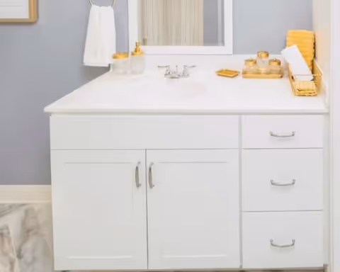White bathroom vanity with sink and mirror, hand towel, and gold-accented toiletries on the countertop.