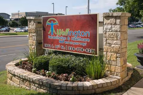 Stone-framed sign for Wellington Rehabilitation and Healthcare amid landscaped shrubs and flowers.
