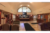 Spacious reception lobby with sofas and chairs facing a central check-in desk beneath a large arched window.