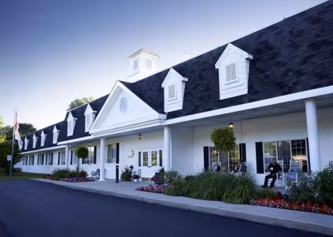 White senior living facility with a long front porch, dormers, and landscaped entrance.
