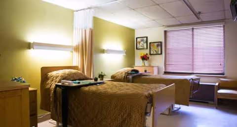 Two hospital-style beds in a shared senior living bedroom with green walls.