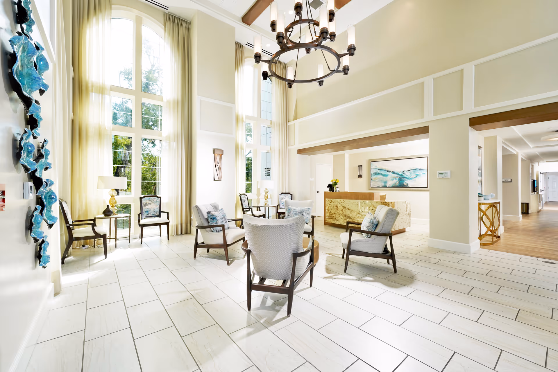 Bright, airy lobby with tall windows, a seating area of chairs and tables, and a reception desk.