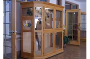 Wooden glass-front display cabinet in an entryway with open glass-paneled doors and a tiled floor.