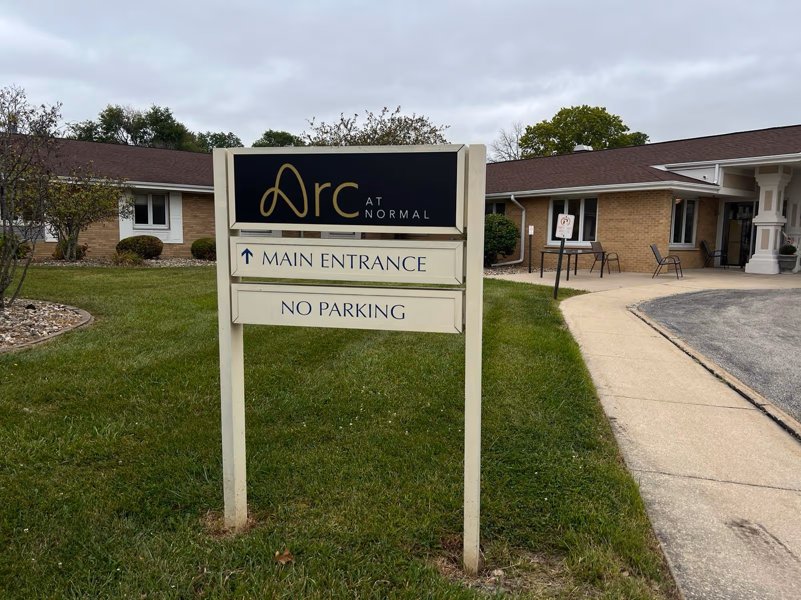 Sign reading 'Arc at Normal' with 'Main Entrance' and 'No Parking' directions on a lawn in front of a single-story facility building.