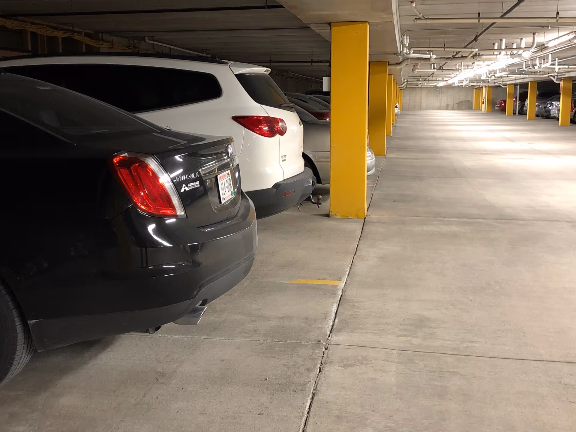 Indoor parking garage with several parked cars along yellow support columns and concrete floor and ceiling.