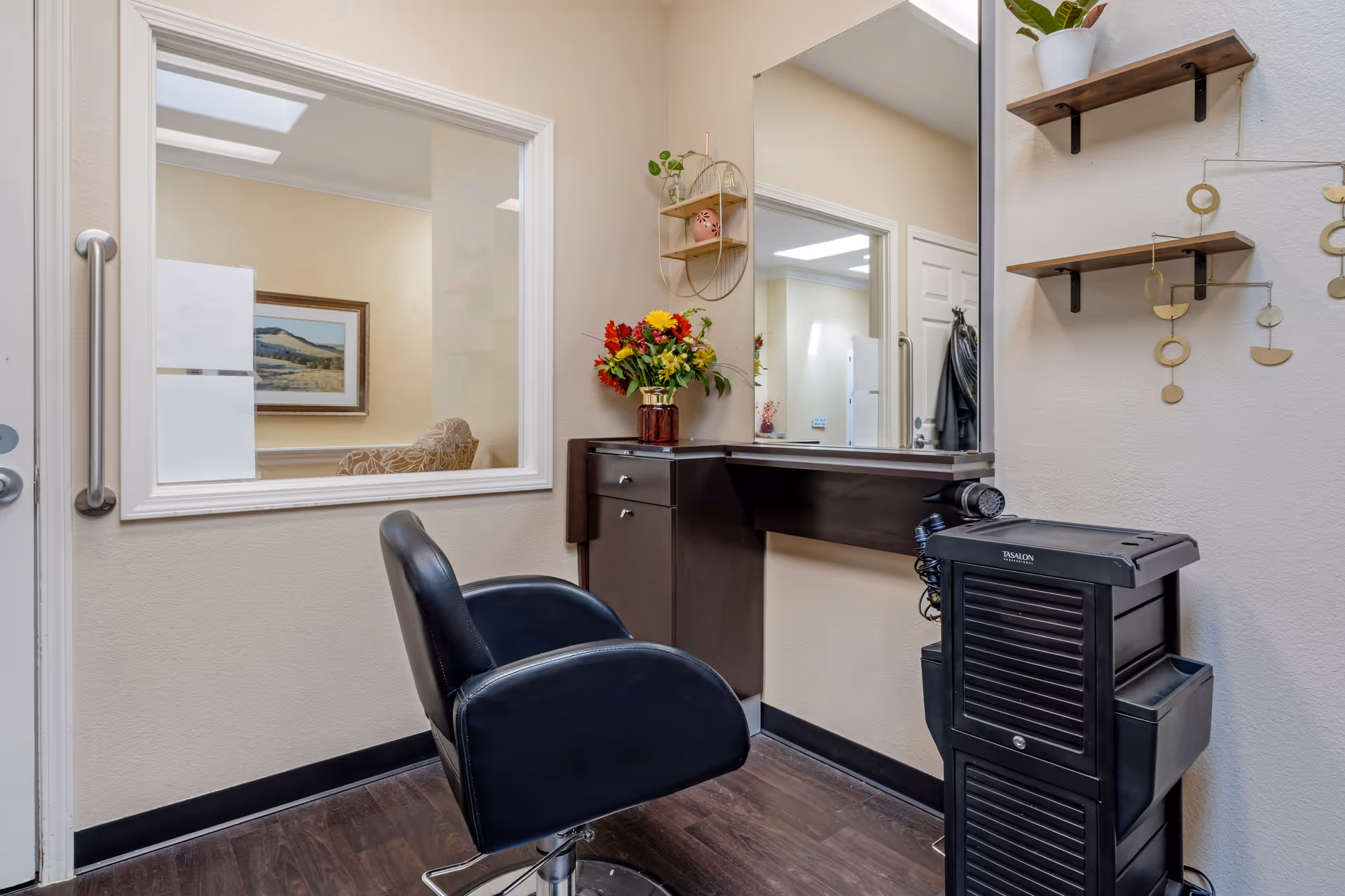 Small salon styling station inside a facility with a black salon chair, mirror, counter, and hair equipment.