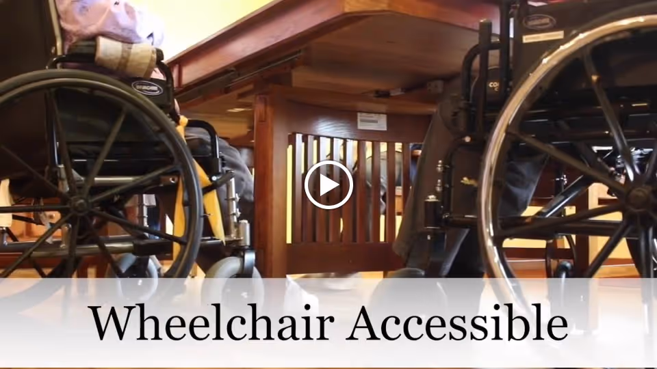 Two wheelchairs positioned at a wooden dining table with the caption 'Wheelchair Accessible' overlaid at the bottom.