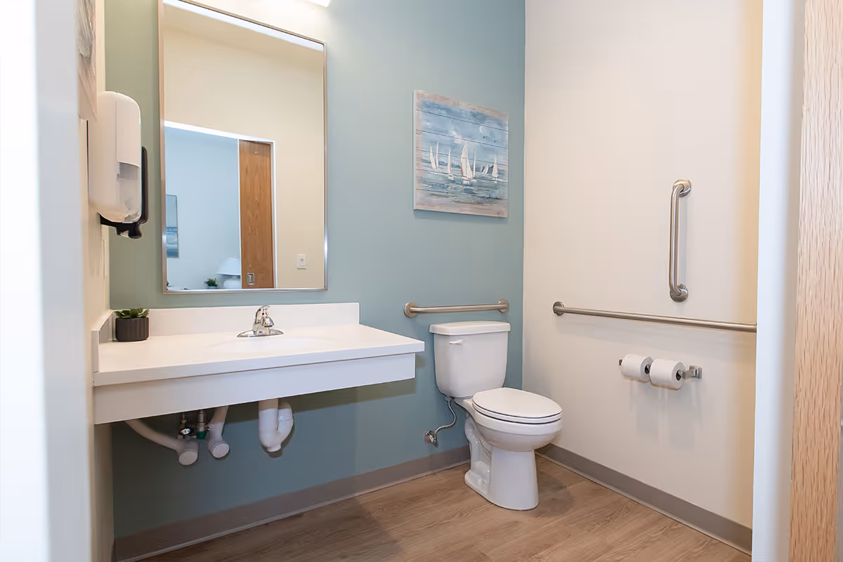 Accessible bathroom with a wall-mounted sink, mirror, toilet, grab bars, and nautical wall art.