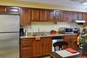 Kitchen featuring wooden cabinets, a stainless steel refrigerator, sink, microwave, and a small dining table with place settings.