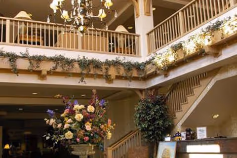 Interior lobby with a grand staircase and balcony, chandelier, and a large floral arrangement.