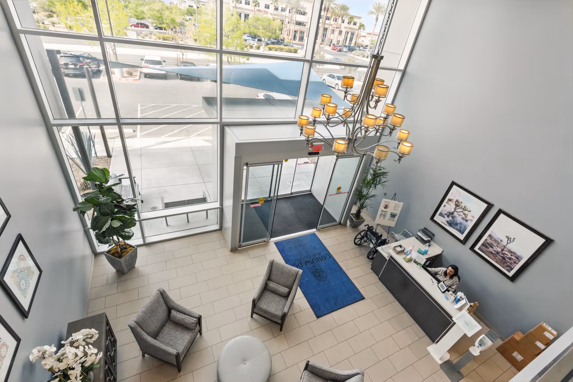 Bright two-story lobby with large windows, a chandelier, reception desk, seating area and entrance doors.