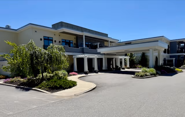 Exterior view of Briarcliffe Preserve Assisted and Independent Living facility showing a modern two-story building with a covered entrance, landscaped greenery, and clear blue sky.