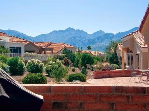 Brick patio and low wall overlooking a landscaped courtyard and tile-roofed homes with mountains in the background.