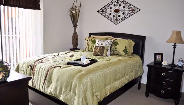 Neat bedroom with a bed dressed in green bedding, two nightstands, a decorative wall hanging, and vertical blinds.