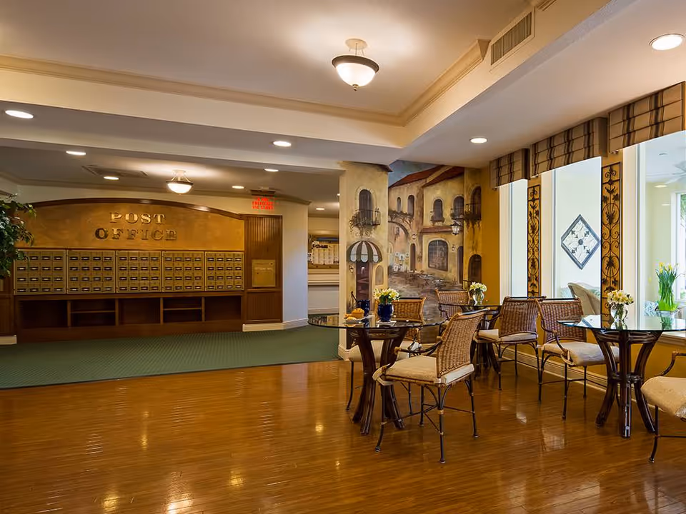 Communal lounge area with a bank of mailboxes labeled 'Post Office', wicker tables and chairs, and a decorative wall mural.