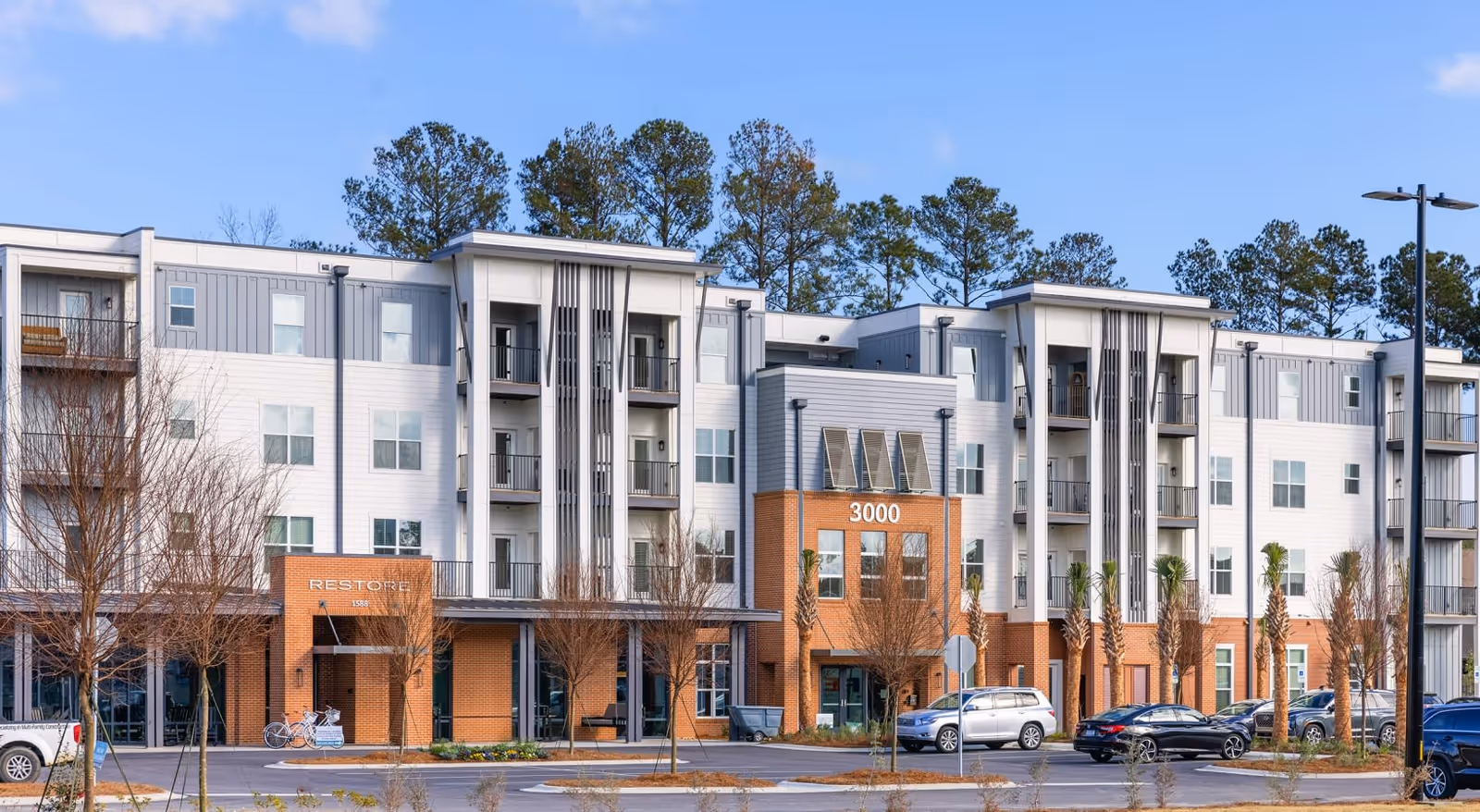 Four-story modern apartment building with brick entrances, balconies and the number "3000" above the main entrance.