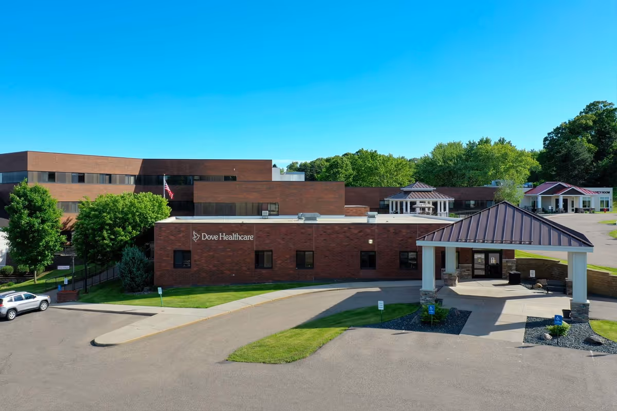 Front exterior of the Dove Healthcare building with a covered entrance, driveway, and surrounding greenery.